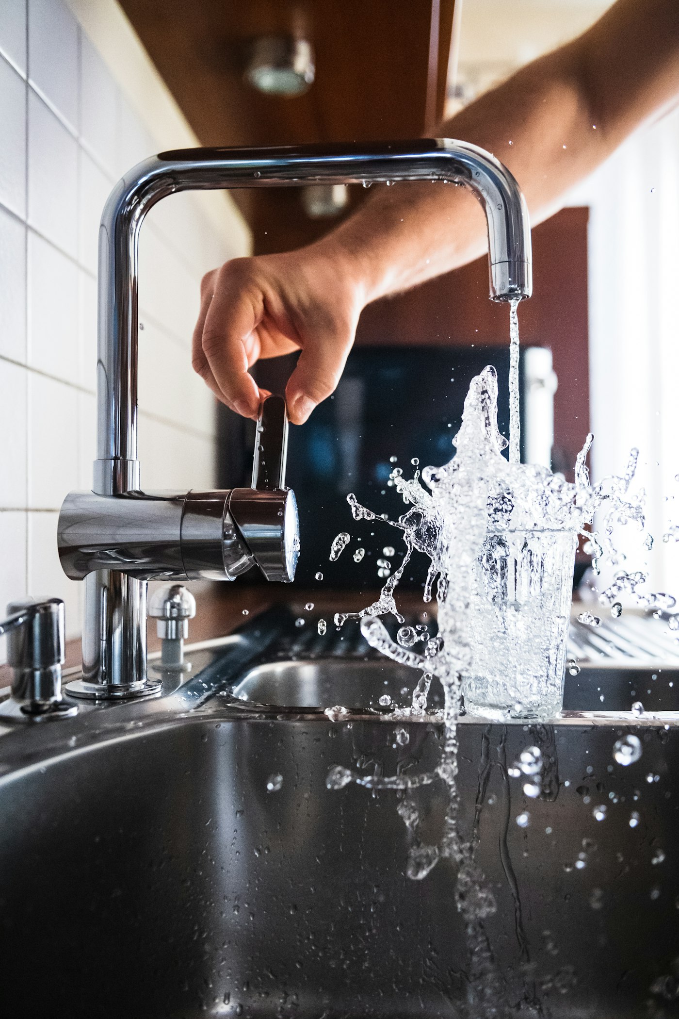 Water rushing from a polished chrome kitchen faucet into a glass